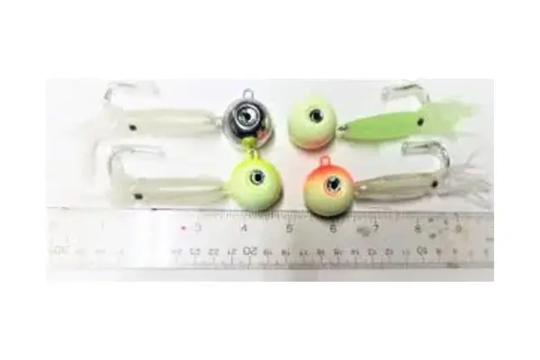 Three fishing lures with colorful, bulbous eyes lie on a white surface next to a ruler showing metric measurements.