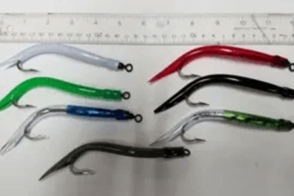 A photo showing seven colorful fishing lures of various colors (white, red, green, blue, black, silver, grey), laid out below a ruler for scale.