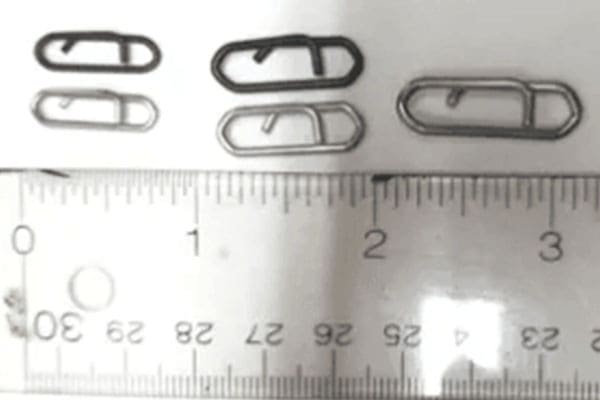 Four paperclips of varying shapes and sizes are aligned above a ruler on a white surface.