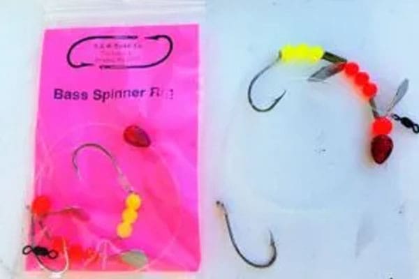 Two fishing lures with hooks, beads, and blades are displayed next to a pink package labeled "Bass Spinner Rig.