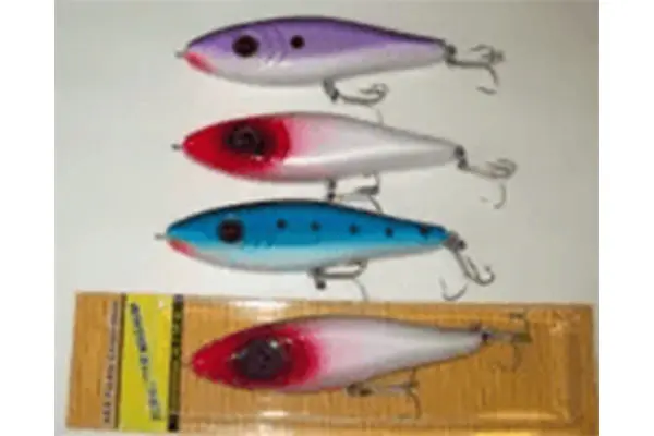 Four fishing lures, three unwrapped in purple, red, and blue, and one in a yellow package with red. All have black eyes and treble hooks.