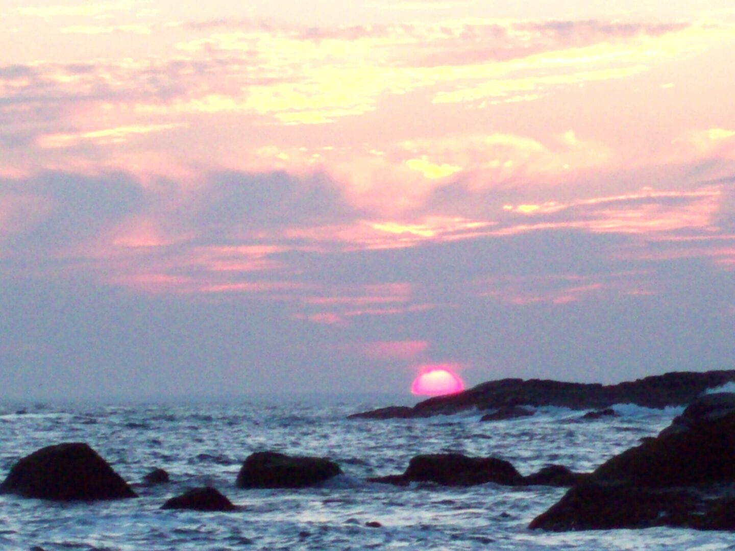 A sunset over the ocean with rocks in the foreground.